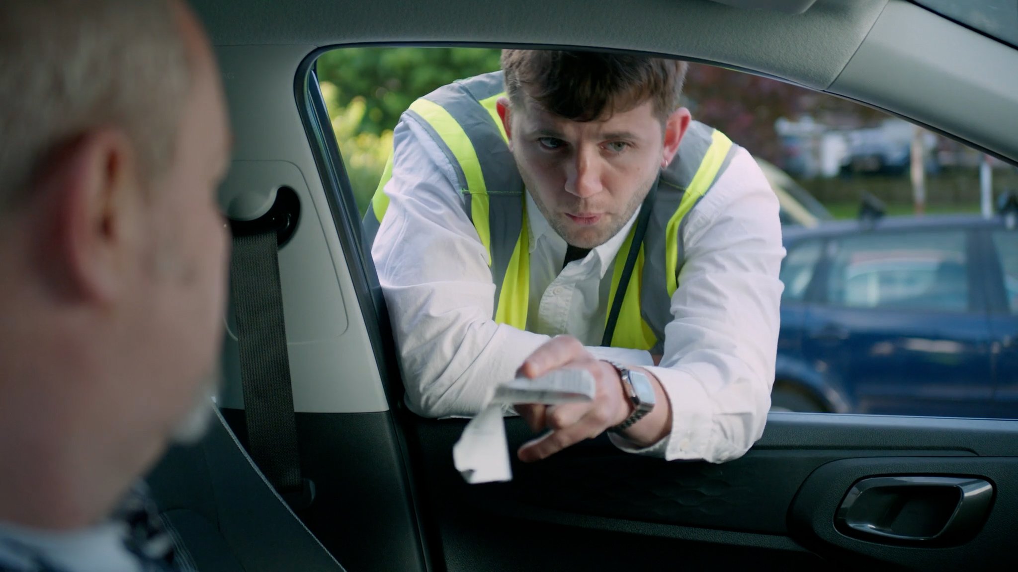 A traffic warden hands a ticket through a car window — still from Ticketed