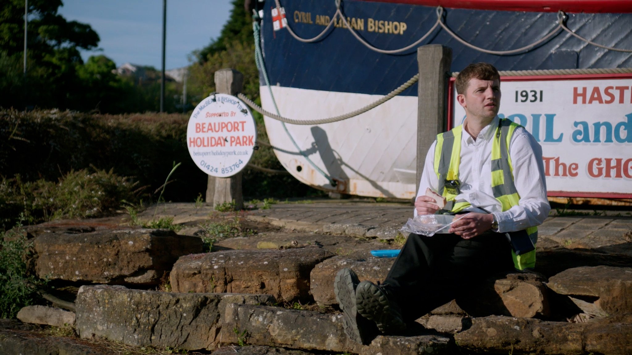 A traffic warden eating lunch outside a seaside holiday park — still from Ticketed